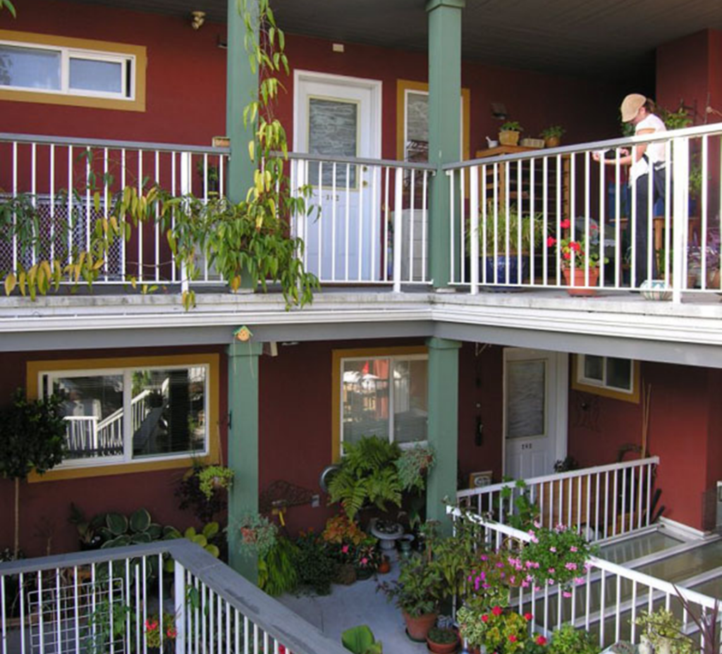 The exterior walkway at Quayside Village Cohousing features places to sit and chat, and is filled with plants.