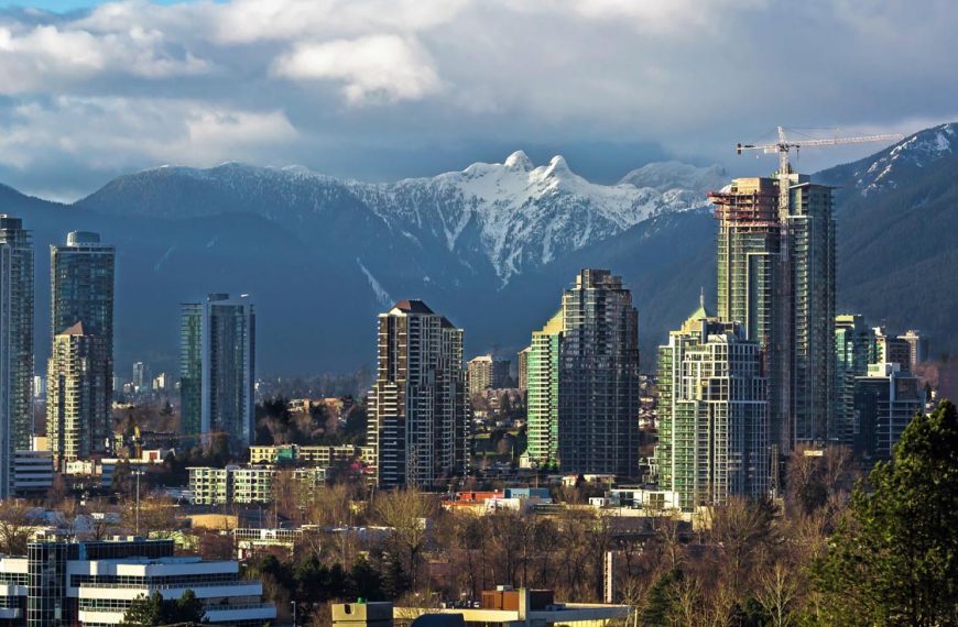 The Coast Mountain range in British Columbia, as seen from Burnaby, BC with tall skyscraper buildings in the foreground.