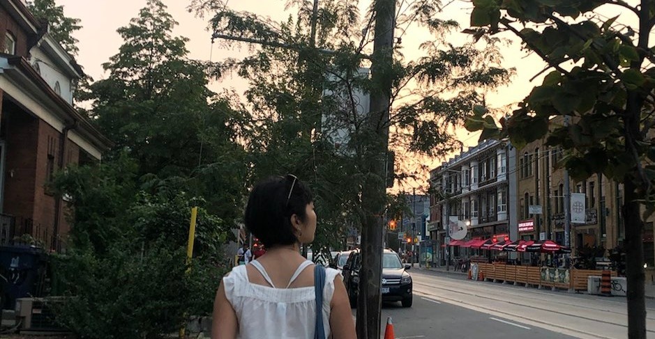 Robyn Lee walks down a tree-lined street at sunset with her back to the camera, looking over her right shoulder.