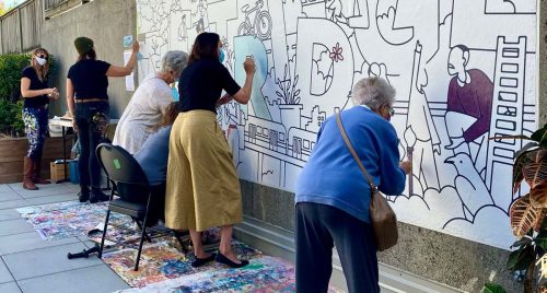 Community members stand working on a public mural in an outdoor space - a great example of a building social connections in a multi-unit building.