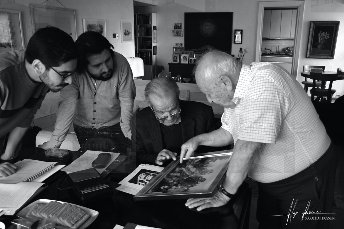 A black and white image of two older, Iranian urban planner professionals along with two younger researchers, looking at photos.