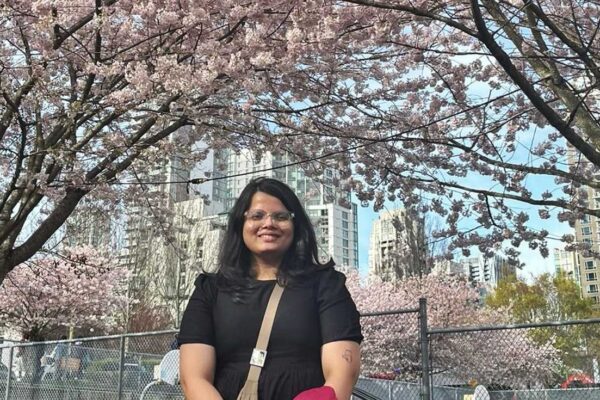 Sreya Ajay stands underneath a natural archway of blooming cherry trees with the Vancouver skyline in the background.