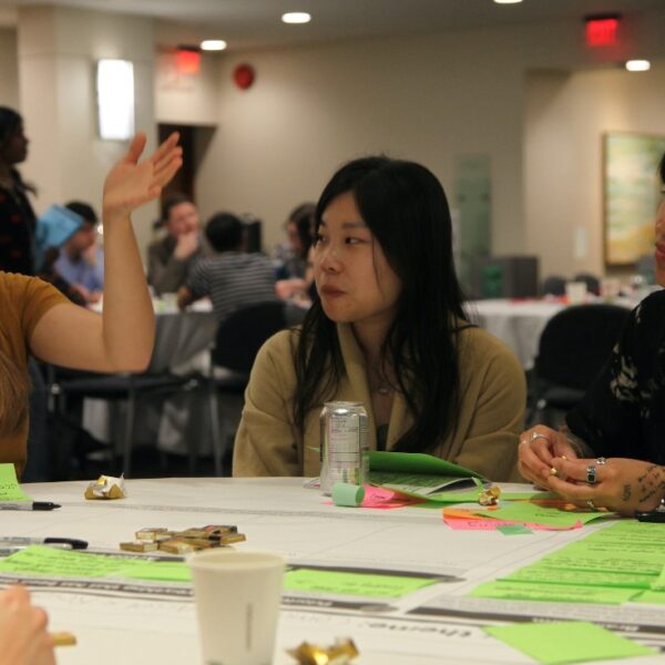 Olivia speaks with her arms raised at a table during the Living Together Symposium in May 2025.