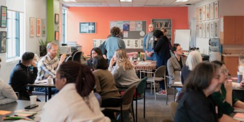 Groups of people gather around small tables in a classroom.