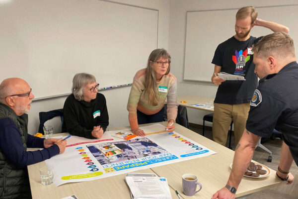 A group of neighbours gathers around a table to make an emergency preparedness plan, while an officer looks on. Photo by Building Resilient Neighbourhoods.