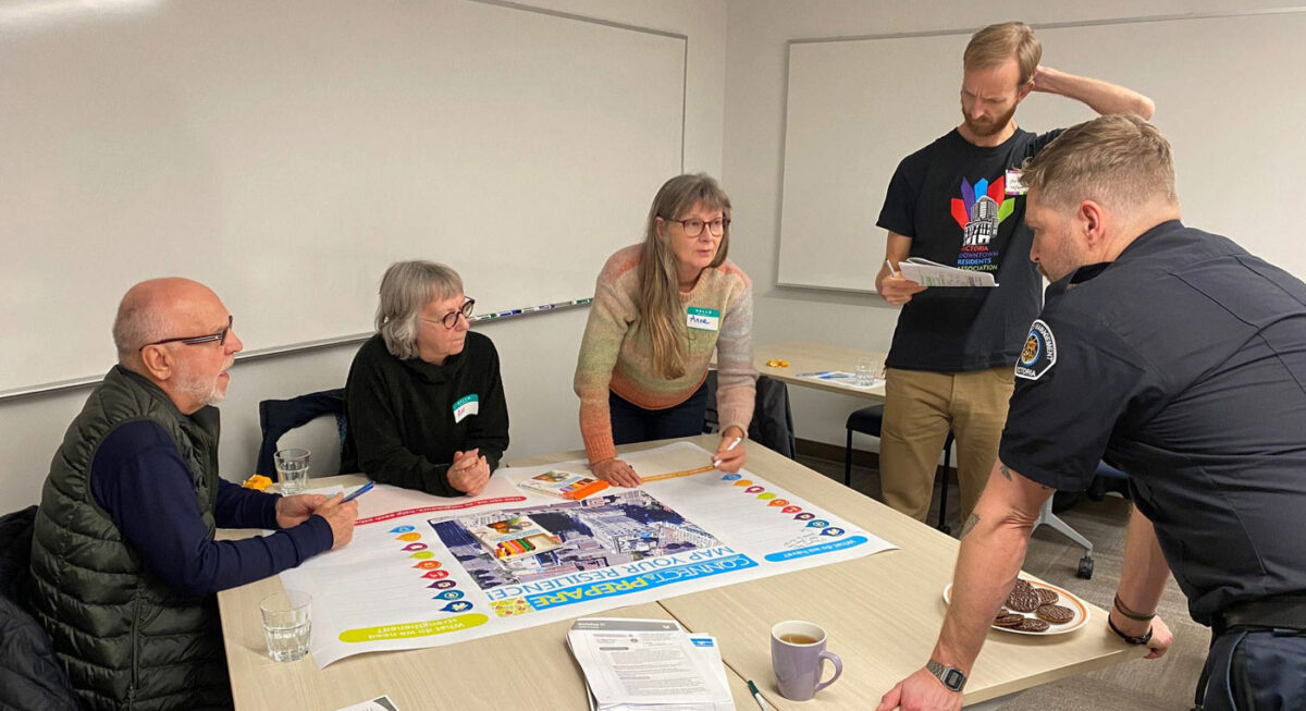 A group of neighbours gathers around a table to make an emergency preparedness plan, while an officer looks on. Photo by Building Resilient Neighbourhoods.