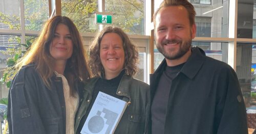 Michelle Hoar stands holding a book titled, 'The Power of Proximity, and she is between Ann-Britt Anderson and a male colleague.