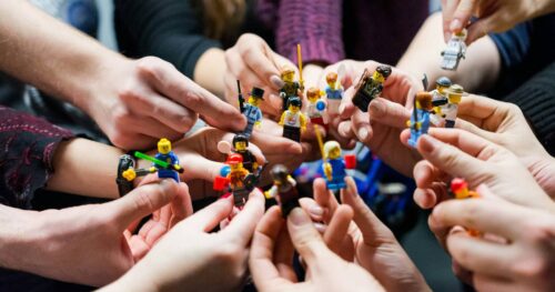 Several Caucasian hands hold Lego figurines together.