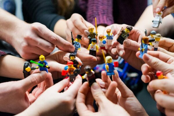 Several Caucasian hands hold Lego figurines together.